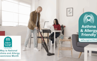 Man vacuuming a bright, modern home with a Asthma & Allergy Friendly® Certified vacuum cleaner, while a woman works nearby—highlighting cleaner indoor air and reduced allergen exposure during Asthma and Allergy Awareness Month.