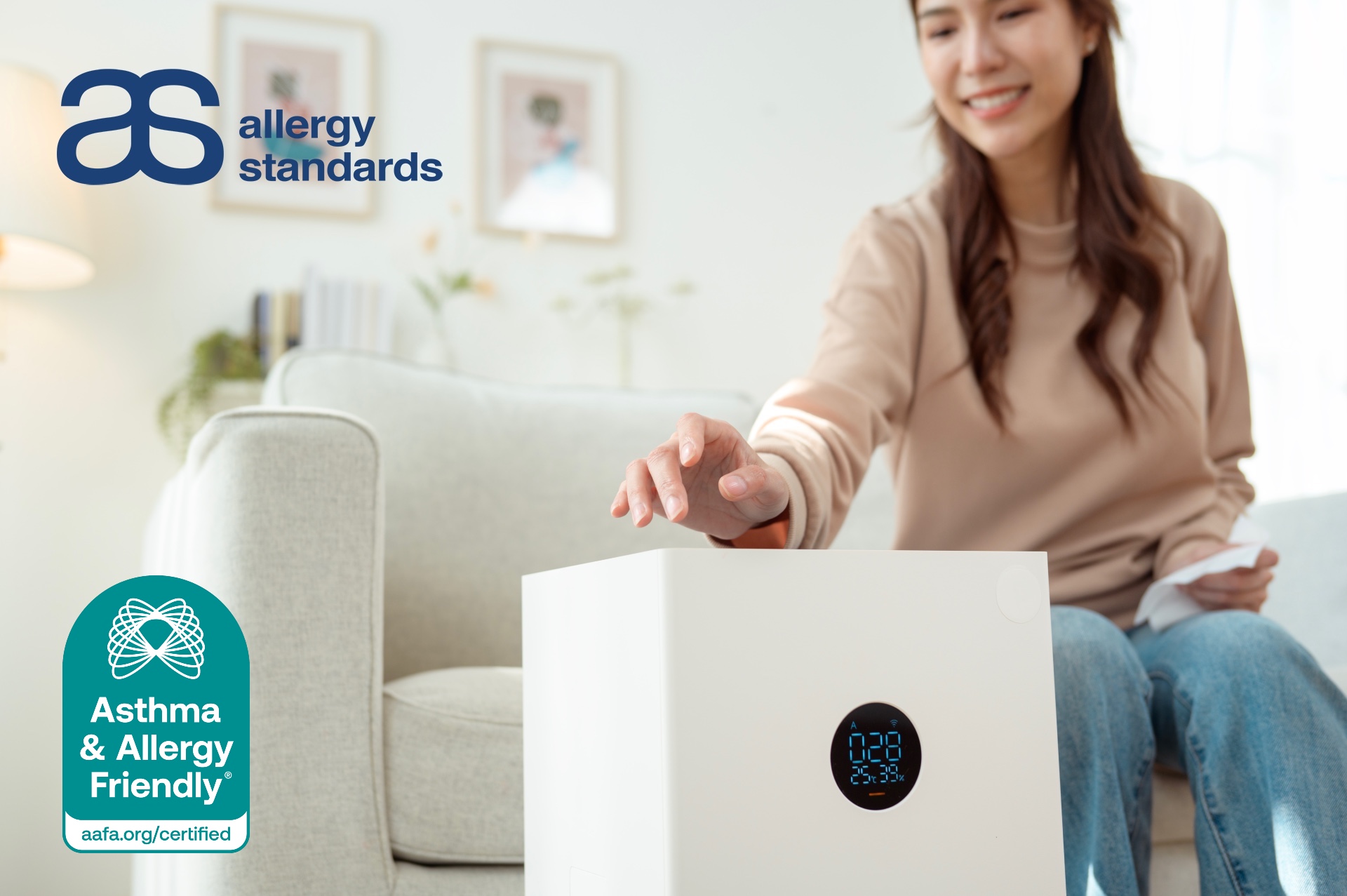 A woman adjusting a compact portable air purifier in her living room, representing the Asthma & Allergy Friendly® Certification Program’s updated standard for smaller certified air cleaners.