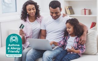 A family sitting together on a sofa shopping online with a laptop, with the Asthma & Allergy Friendly® Certification Mark displayed in the foreground