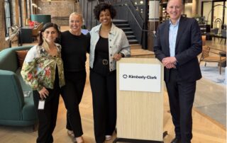 Leah McInerney, Sharnell Weathersby, and Dr. John Ryan standing beside a Kimberly-Clark sign at Kimberly-Clark's Chicago office
