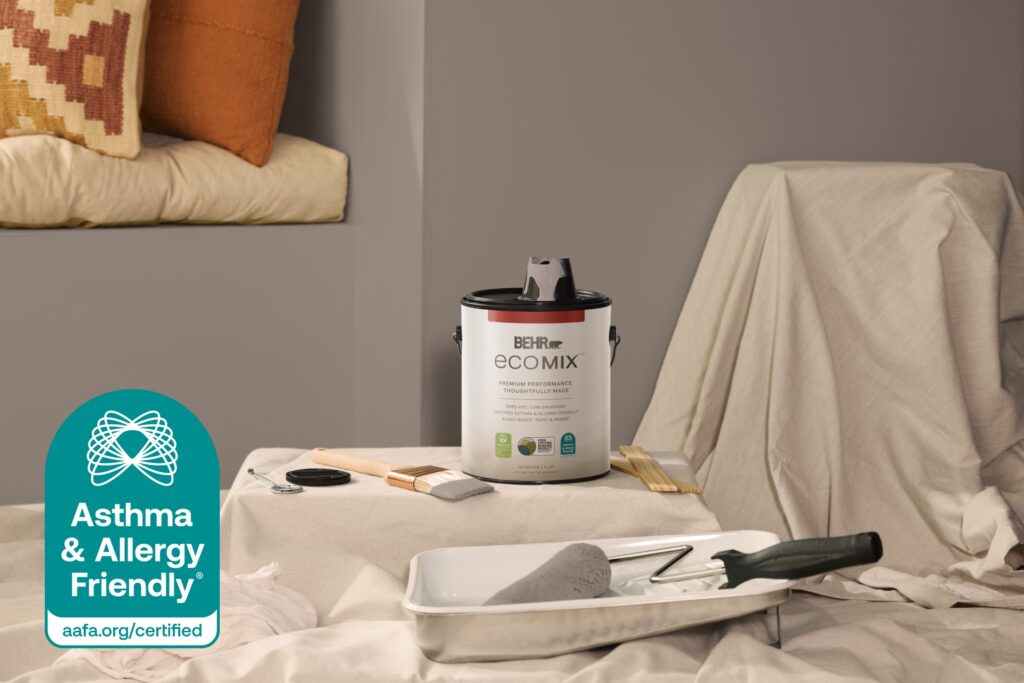 A can of BEHR ECOMIX Interior Paint & Primer in Flat with a brush, roller tray and drop cloth, and the Asthma & Allergy Friendly® Certification Mark